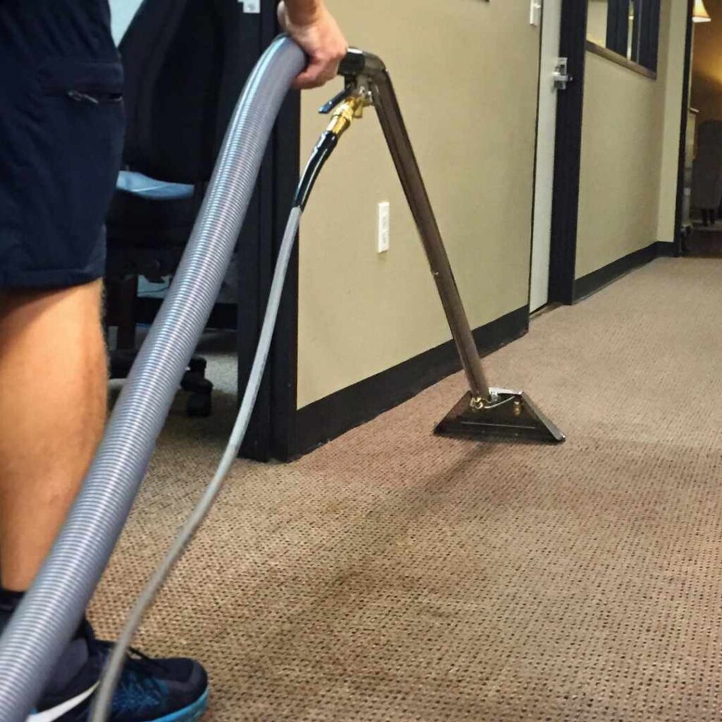Professional carpet cleaning in an office hallway using a commercial extraction wand to remove dirt and allergens.