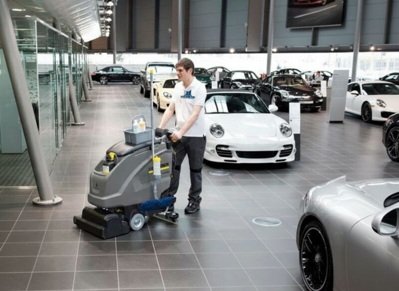 Elite Sani Pro technician using a professional floor scrubber to polish the showroom floor of a luxury car dealership.