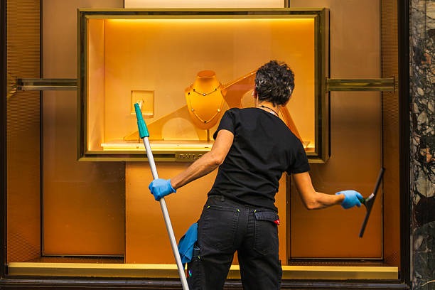 professional cleaner performing commercial window cleaning on a luxury retail storefront display using professional cleaning equipment.