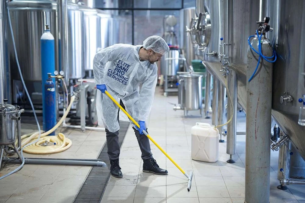 Elite Sani Pro professional in protective gear using a squeegee to clean floors in an industrial manufacturing or brewery facility.